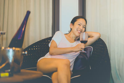 Portrait of young woman sitting on sofa drinking red wine at home