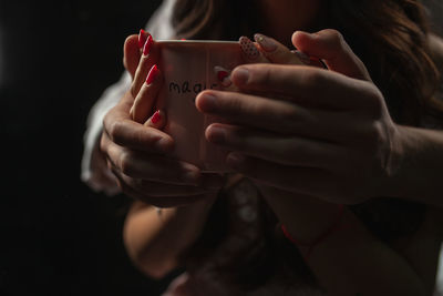 Cropped hands of man with girlfriend holding bowl against black background