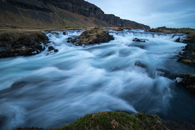 Scenic view of waterfall by sea against sky