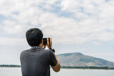 Rear view of man photographing against sky