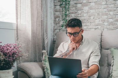 Young woman using laptop while sitting on sofa at home