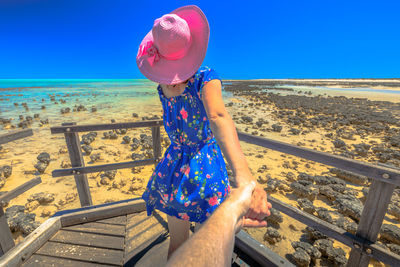 Cropped image of man holding woman hand standing on footbridge against sea and sky