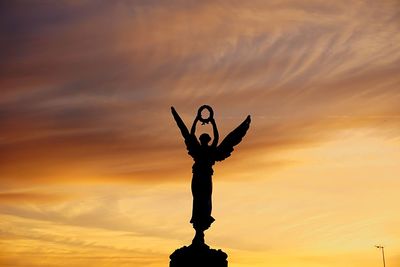 Low angle view of silhouette statue against orange sky