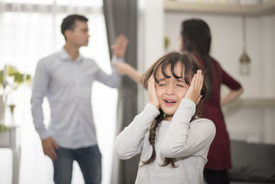 Close-up of girl crying while parents fighting in background at home