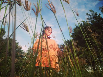 Portrait of girl standing by plants against sky