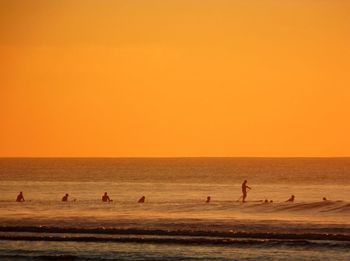 Silhouette people on beach against orange sky