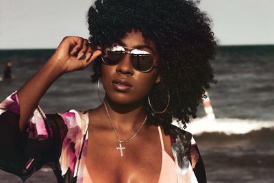 Young woman wearing sunglasses standing at beach against cloudy sky