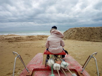 Rear view of person sitting at beach against sky