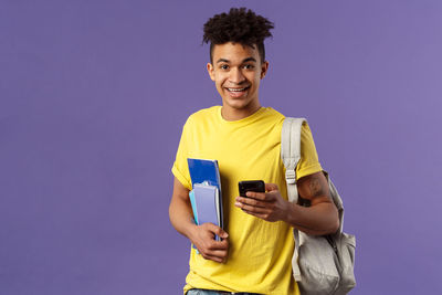 Portrait of smiling young man using smart phone against gray background