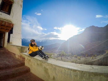 Full length of woman sitting on retaining wall against mountains