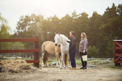 Side view of farmer stroking horse while standing by woman on field