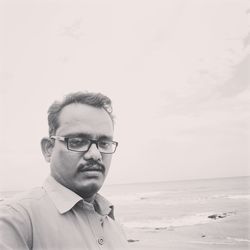 Portrait of man wearing eyeglasses at beach against sky