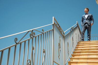 Low angle view of man standing on staircase against clear sky