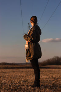 Full length side view of woman standing on land against sky during sunset