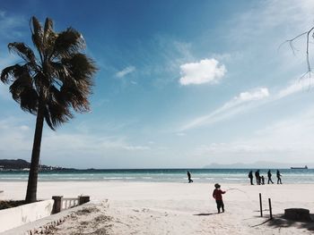 Tourists on beach against cloudy sky