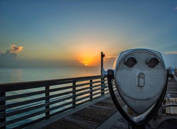 Coin-operated binocular on pier over sea against sky during sunset