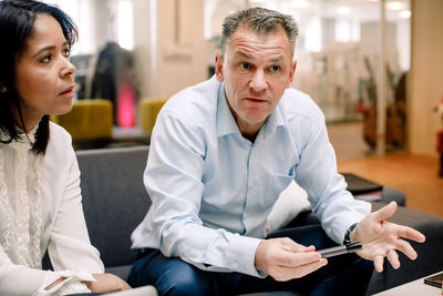 Serious mature professional gesturing while looking away by businesswoman at work place