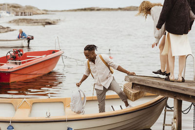 Smiling man helping female friends boarding boat by harbor