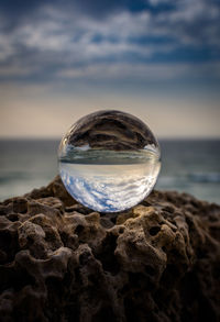 Close-up of crystal ball on beach against sky