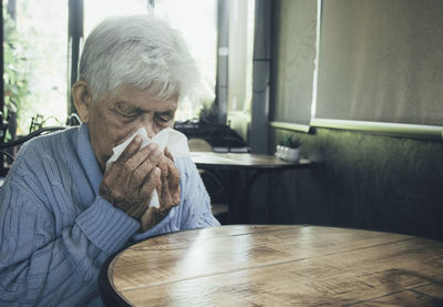 Old person coughing covering mouth with a tissue on a house interior. she has flu, allergy symptoms.