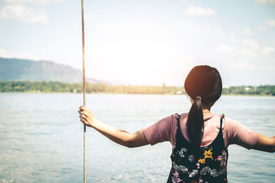 Rear view of woman swinging by lake