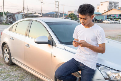 Young man using mobile phone while standing on car