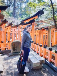 Full length side view portrait of young woman standing against shrines in forest