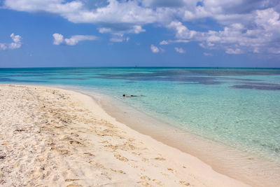 Woman swimming in sea against cloudy sky