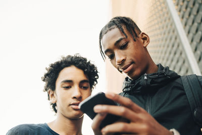 Low angle view of teenage boy showing mobile phone to friend in city