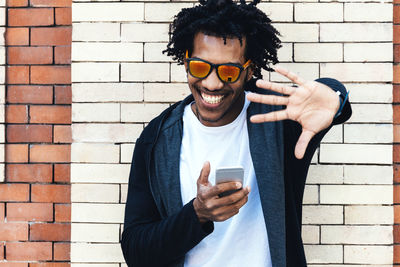 Young man using mobile phone while standing against brick wall