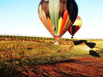 Hot air balloon flying over field against clear sky