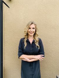 Portrait of a smiling young blonde woman standing against wall