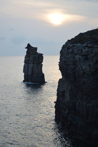 Rock formation in sea against sky during sunset