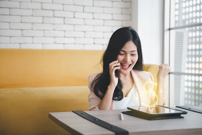 Young woman using phone while sitting on table