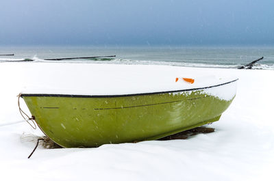 Boat moored at snow covered beach by sea