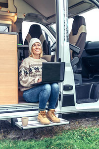 Woman teleworking sitting in the door of a camper van