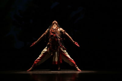Full length of man wearing shiva costume performing on stage in dark