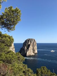 Rock formation by sea against clear blue sky