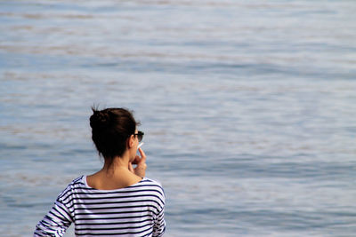 Rear view of woman smoking while standing at lakeshore against sky