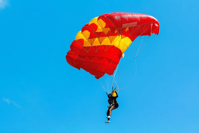 Low angle view of man paragliding against clear blue sky