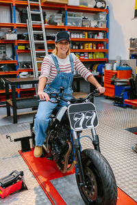 Portrait of mechanic woman sitting over motorcycle on factory