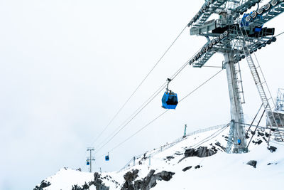 Low angle view of overhead cable car on snow covered mountains against sky