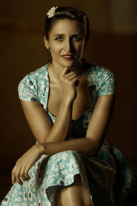 Portrait of smiling woman with hand in chin sitting in darkroom