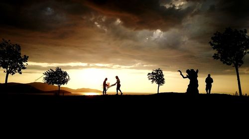 Silhouette people standing by tree against sky during sunset