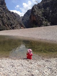 Person on red rock in mountains against sky