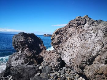 Rock formations on shore against clear blue sky