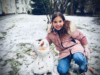 Portrait of smiling girl with snowman outdoors