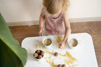 Toddler girl playing with grain, nuts, pasta, rice sitting at table.sensorial early kid development