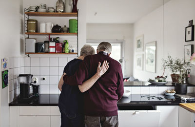 Rear view of retired senior couple standing in kitchen at home