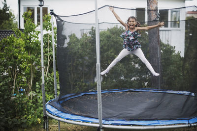 Portrait of excited girl jumping on trampoline at yard